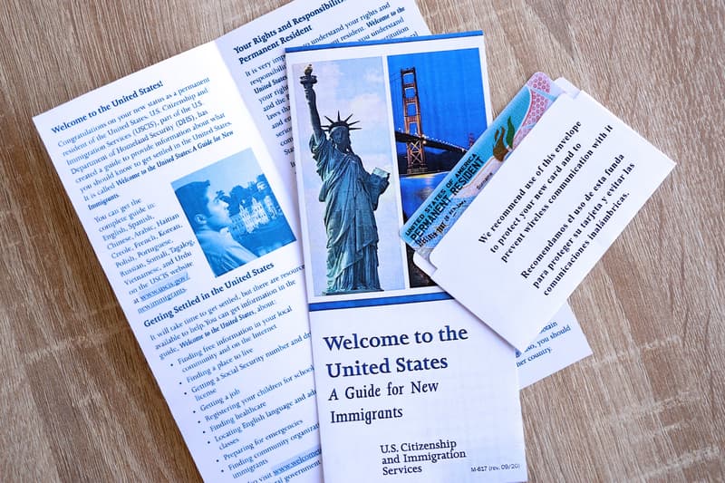 Permanent resident green card in envelope and guide for new immigrants lies on wooden table